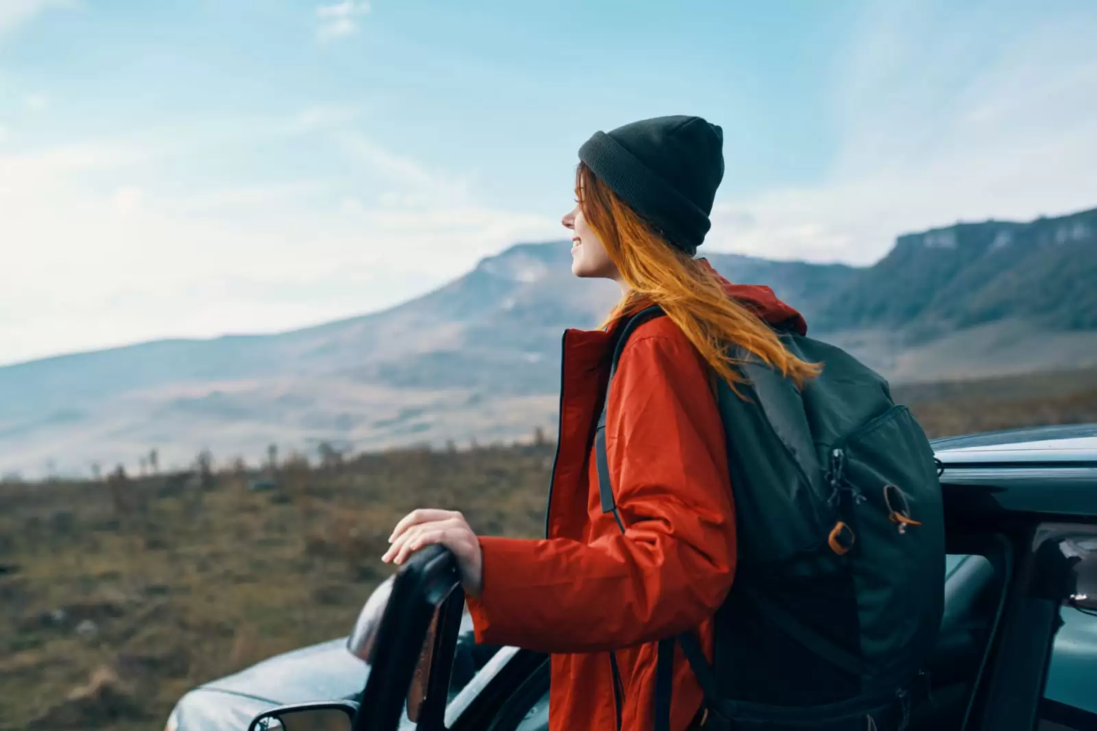Una chica con chaqueta naranja y mochila junto a un coche con Seguro de garantía