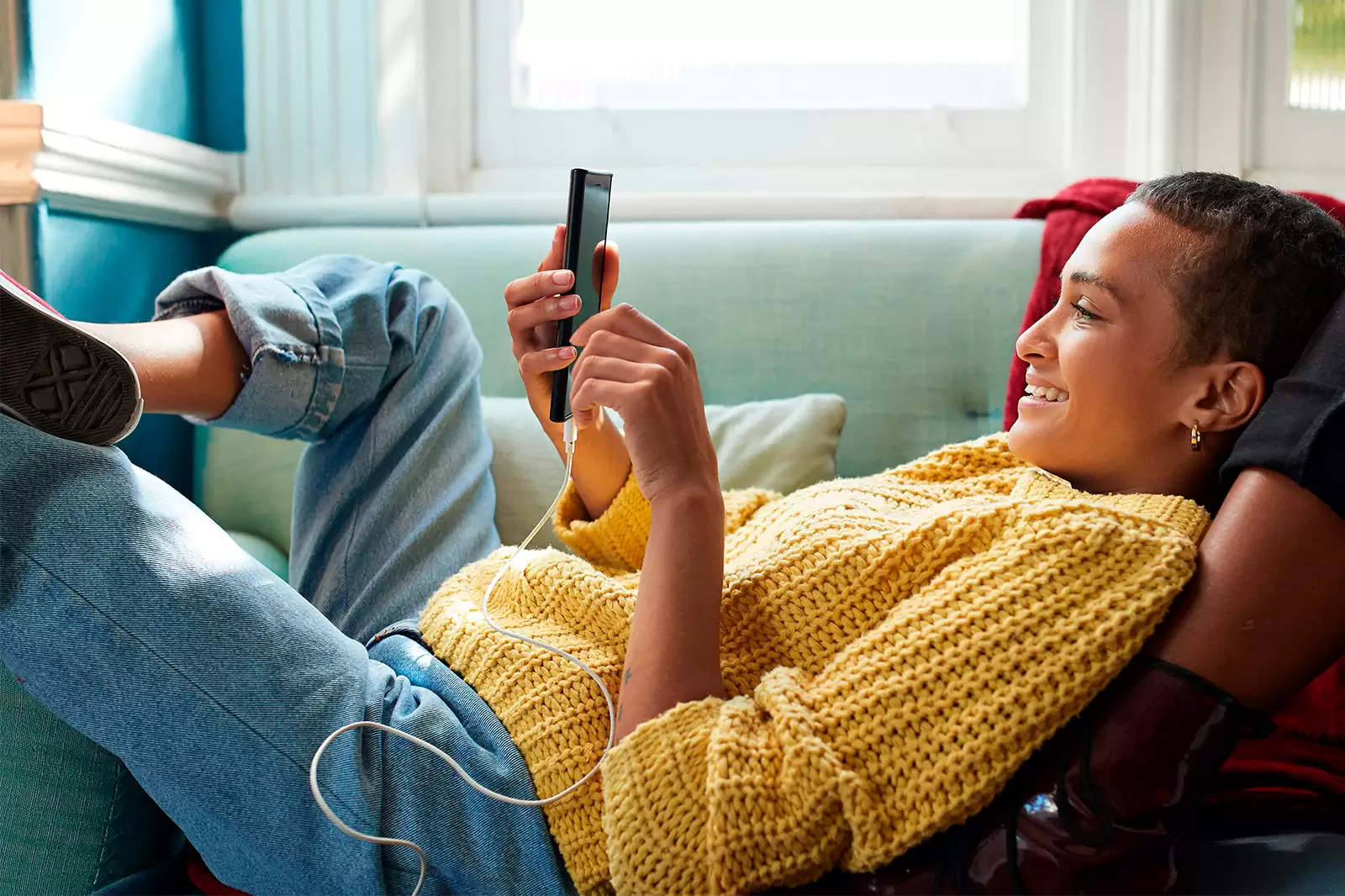Chica con jersey amarillo recostada en un sofá mirando el móvil