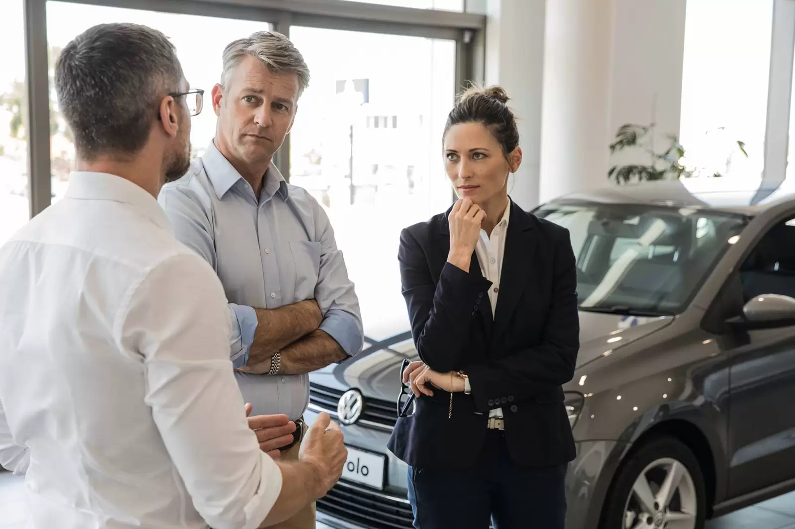 Dos hombres una mujer hablando delante de un Volkswagen Polo en un concesionario
