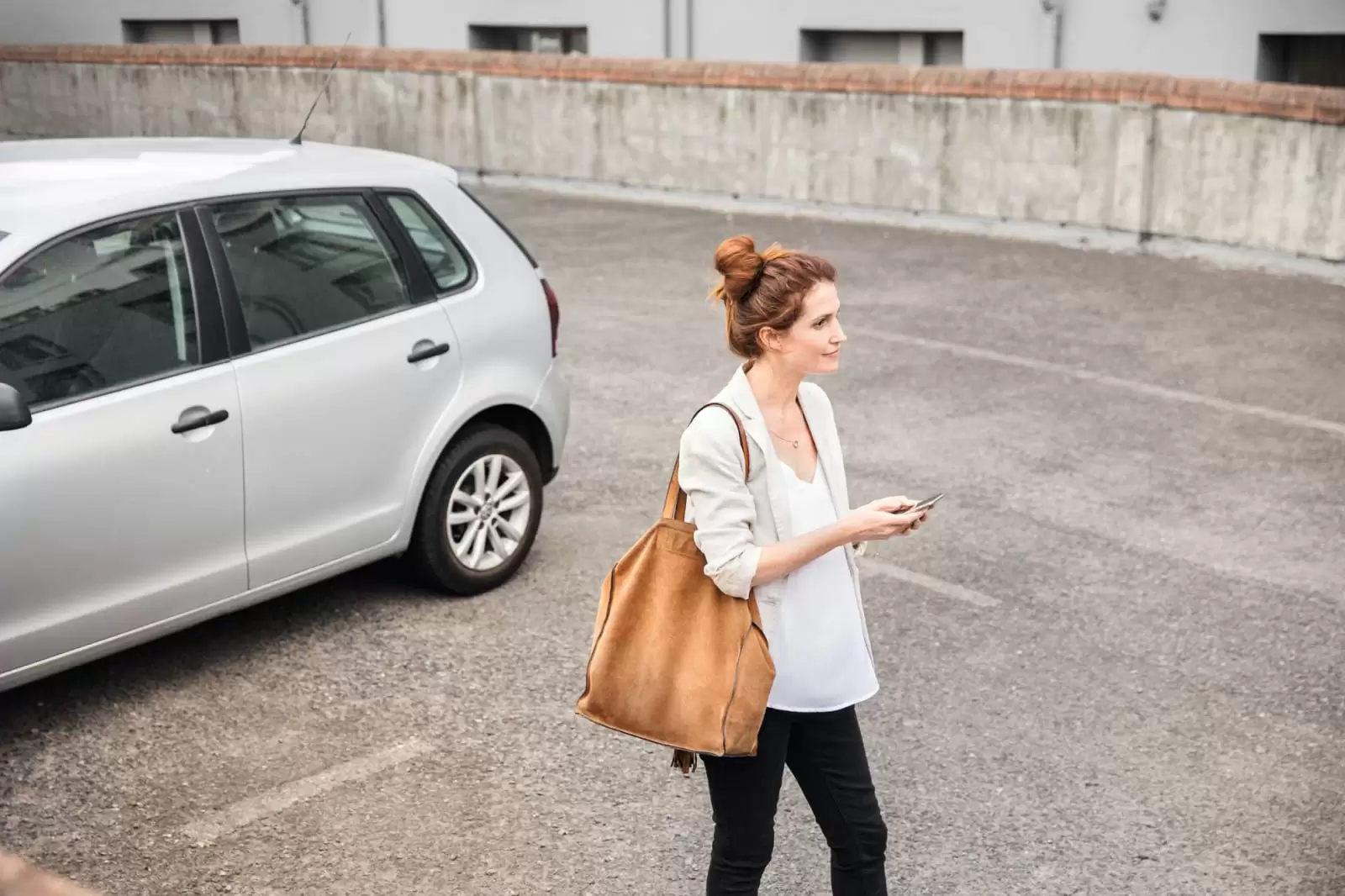 Una mujer con un móvil en la mano delante de un coche de suscripción en un parking
