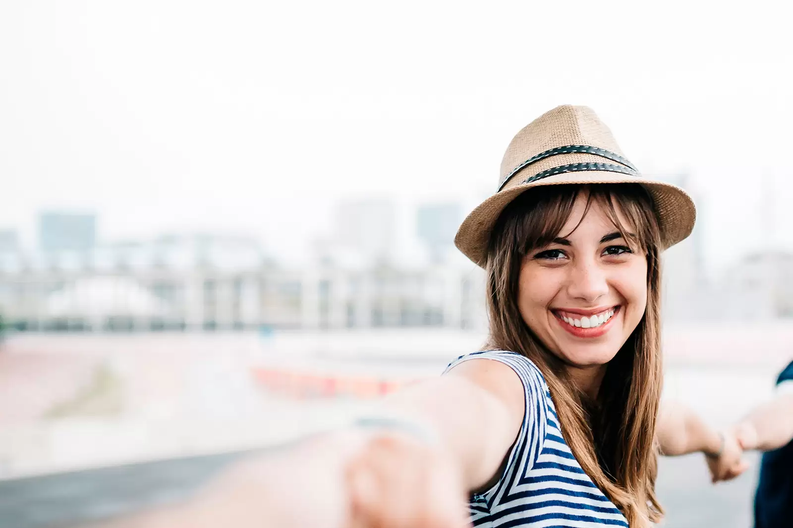 Chica joven sonriendo con sombrero mirando de frente tomada de las manos