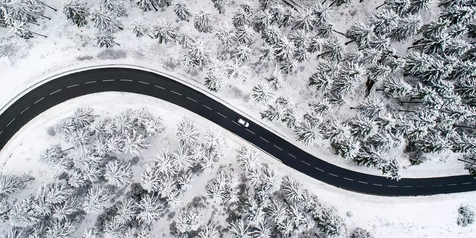 Coche visto desde arriba en una carretera nevada en el bosque