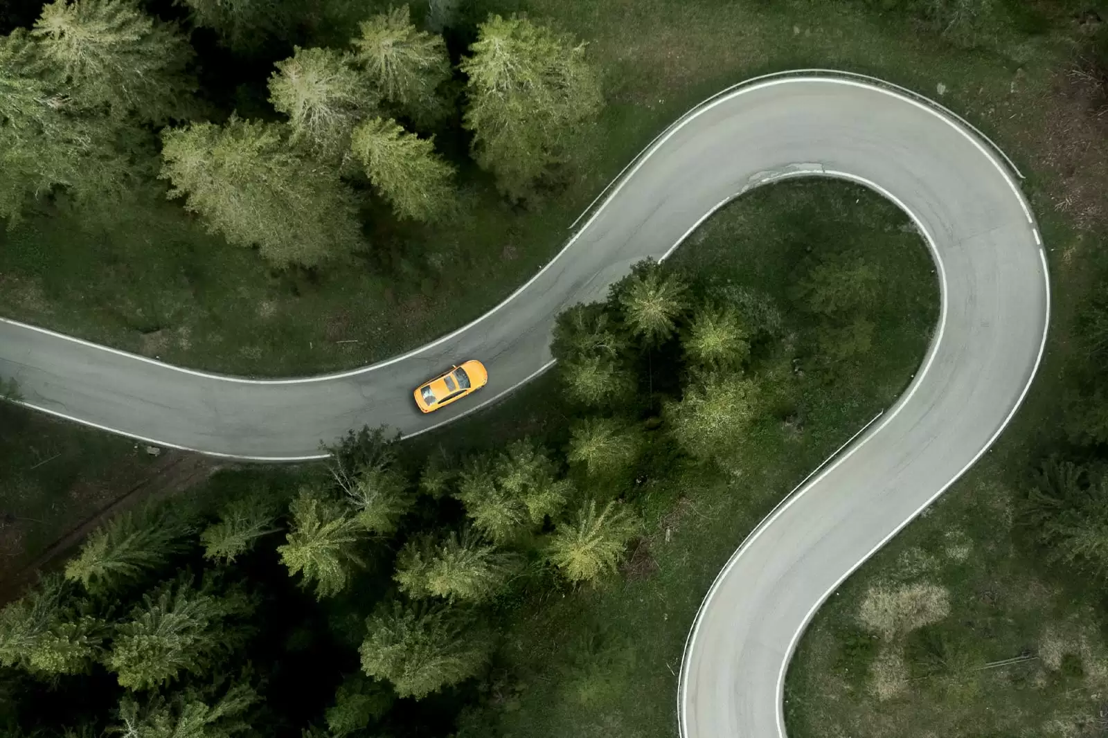 Un coche de Renting amarillo visto desde arriba en una carretera en el bosque