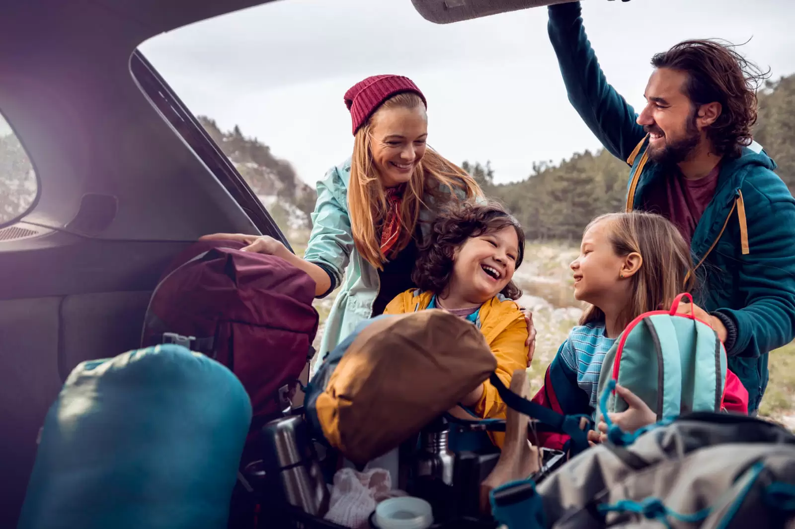 Una familia de excursión sacando mochilas de un coche de compra flexible en la montaña