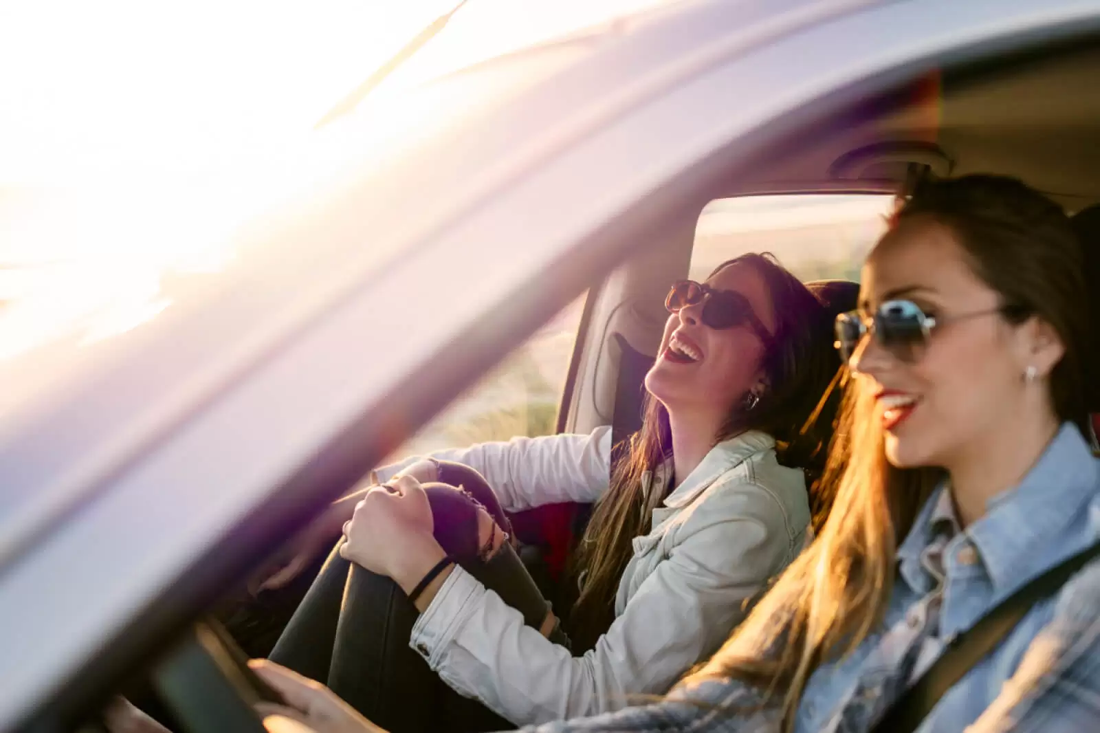 Dos chicas sonriendo dentro de un coche de Renting al atardecer