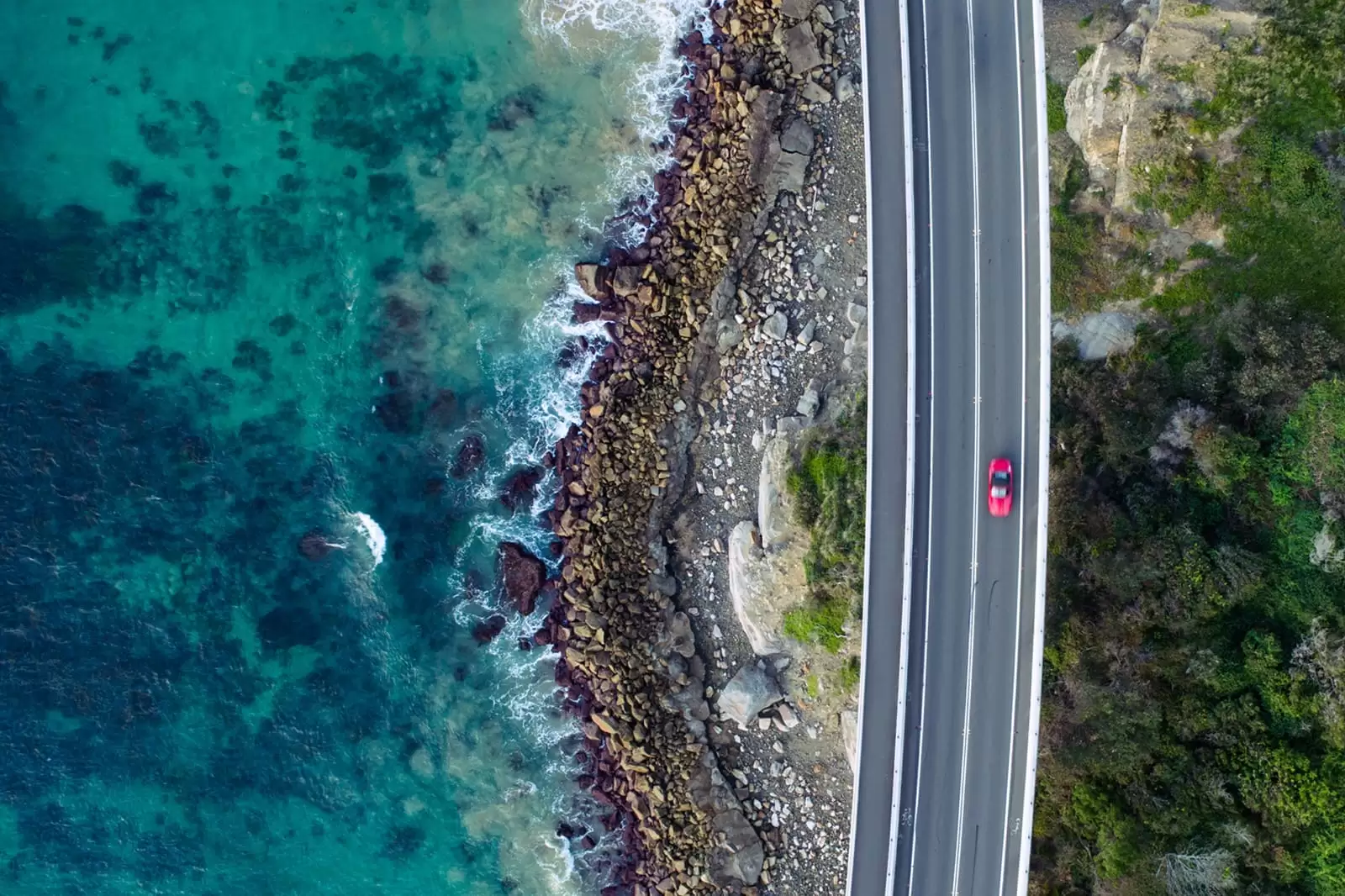 Un coche de Renting rojo en una carretera junto al mar visto desde arriba